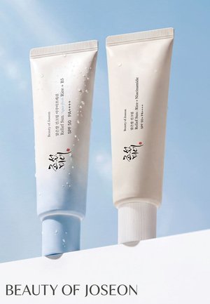 Due tubi di crema solare Beauty of Joseon con SPF 50 e gocce d'acqua su uno sfondo di cielo blu.