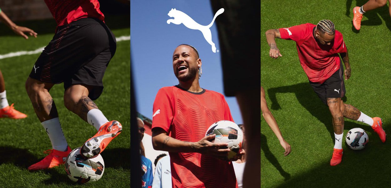 Rotes Puma-Trikot mit strukturiertem Muster, schwarze Shorts und orangefarbene Stollenschuhe. Im Hintergrund sind ein Fußball und ein auffälliges Puma-Logo zu sehen.