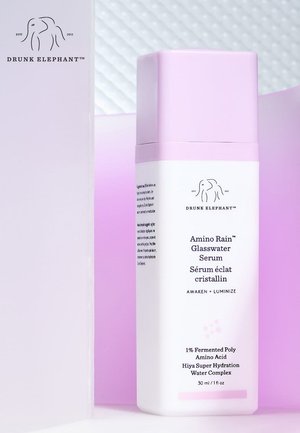 Drunk Elephant Amino Rain Glasswater Serum bottle with pink cap on a soft purple and white background.
