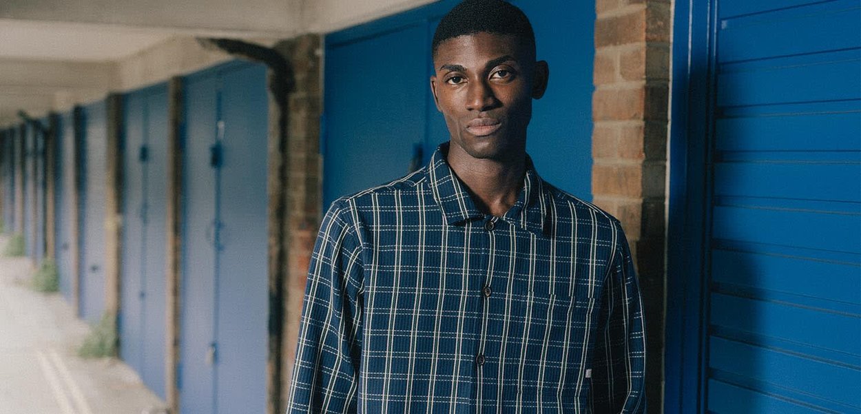 Marineblaues Karohemd mit Button-Down-Kragen und kurzen Ärmeln, aus strukturiertem Stoff. Dagegen stehen blaue Aufbewahrungseinheiten.