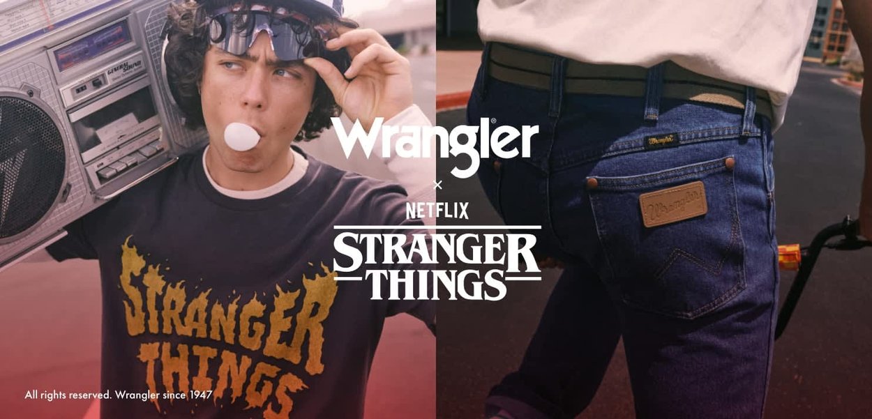 Svarte T-skjorte med gul tekst "Stranger Things"; blå denimjeans med en beige lærlapp; en sølvfarget boombox holdt på venstre skulder.