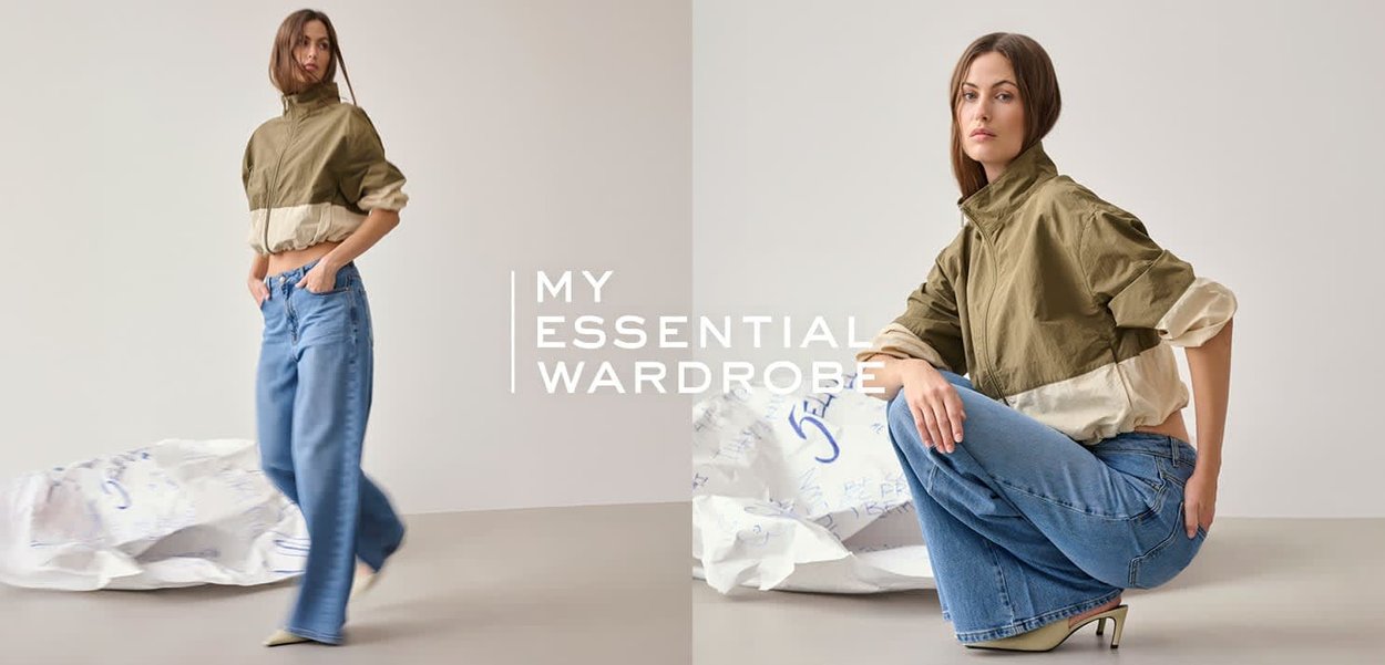 Frau in einer zweifarbigen Jacke in Olive und Beige mit weit geschnittenen blauen Jeans, die vor einem schlichten Hintergrund stehend und hockend posiert.