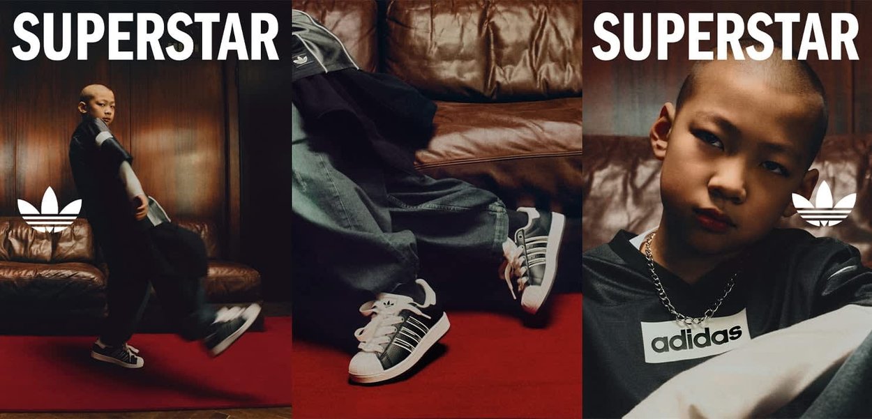 Dziecko ubrane w odzież i buty Adidas pozuje pewnie na czerwonej podłodze, z brązową skórzaną kanapą i napisem "SUPERSTAR" nad sobą.