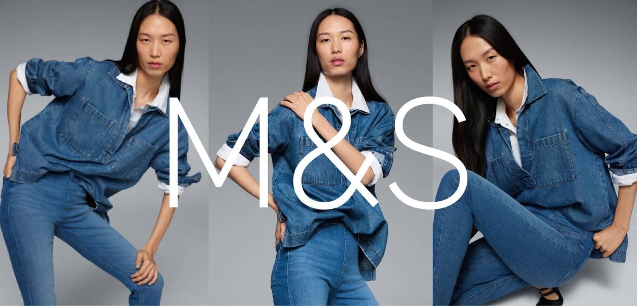 Denim shirt and jeans in medium blue. Shirt features a white collar and front pocket. Model poses with hands on hips and crossed legs.