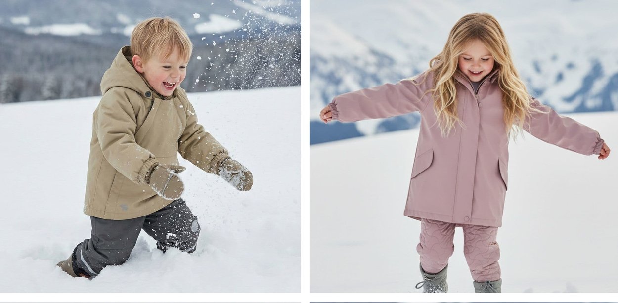 Ein Junge wirft im Knien Schnee und lächelt; ein Mädchen balanciert mit ausgebreiteten Armen, beide tragen Winterkleidung in einer verschneiten Landschaft.