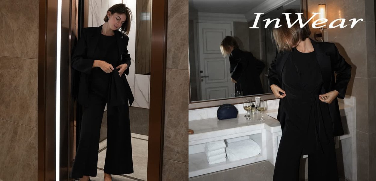 Black tailored suit with wide trousers and a wrap-top design, made from a smooth fabric. Set against a stylish interior with vanity.
