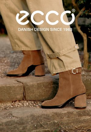 Stivali alla caviglia in suede marrone con punta quadrata, tacco a blocco spesso e una cinghia con fibbia argentata. Indossati con pantaloni croppati color khaki.