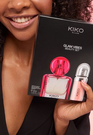 Persona sorridente tiene il KIKO Milano Glam Vibes Beauty Set con profumo e gloss per labbra in confezione nera.