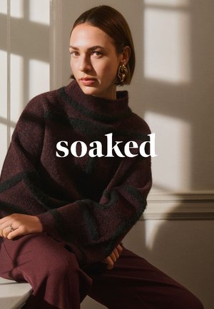 Braun-schwarz gestreifter Strickpullover mit hohem Kragen, ausgestattet mit weiten Ärmeln. Tiefrote Hosen. Weiche Textur und lockere Passform.