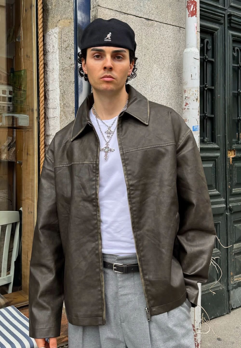 Pruun kunstnahast jakk terava kraega, kantud valge särk üle. Ühendatud hallide pükste ja musta mütsiga, lisaks kihilised hõbedased kaelakeed.