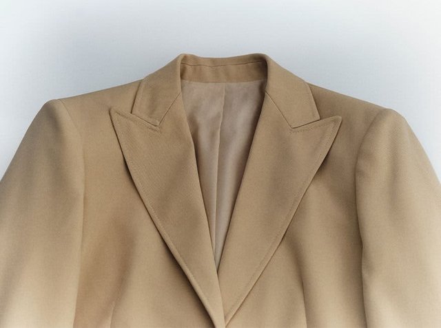 Beige blazer with a notched collar, smooth texture, and structured shoulders. Interior lined in a lighter colour. No visible fastenings.