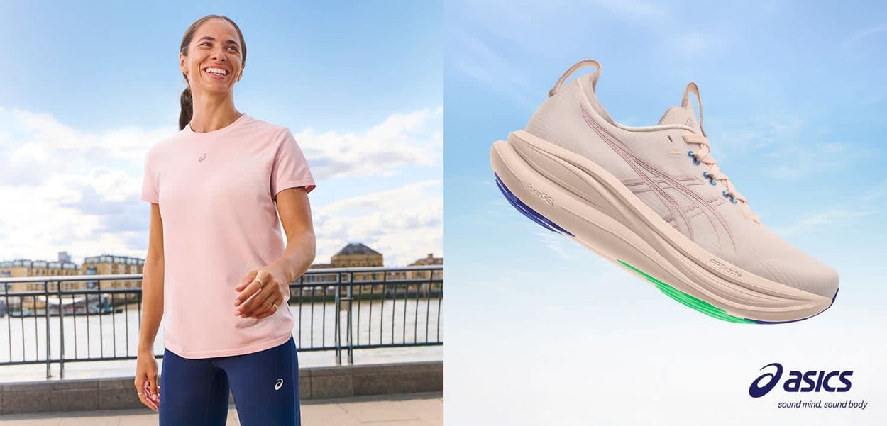Lachende vrouw in een roze shirt en marineblauwe legging staat aan de oever van de rivier; een beige ASICS hardloopschoen zweeft tegen de blauwe lucht met het merklogo eronder.