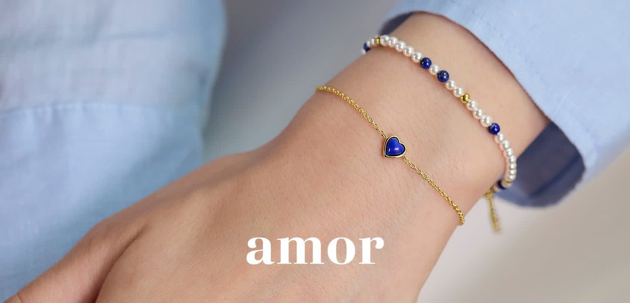 Bracciale d'oro con un ciondolo a forma di cuore blu e un braccialetto di perline che alterna perle e perline blu su un polso.