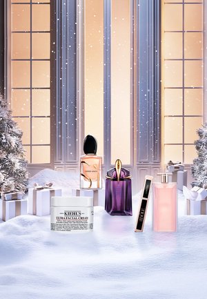 Collection of fragrance bottles and a cream jar. Features include varied shapes, colors (purple, pink, black), and labels. Snowy background with gifts.