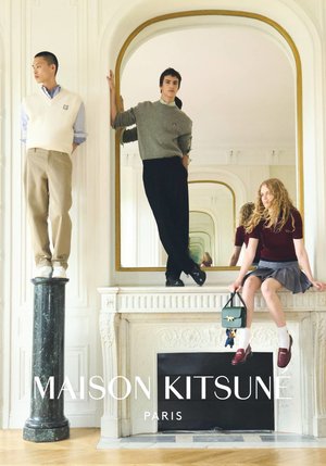 Three people pose in stylish casual outfits inside a bright room with ornate fireplace and large mirror reflecting them.