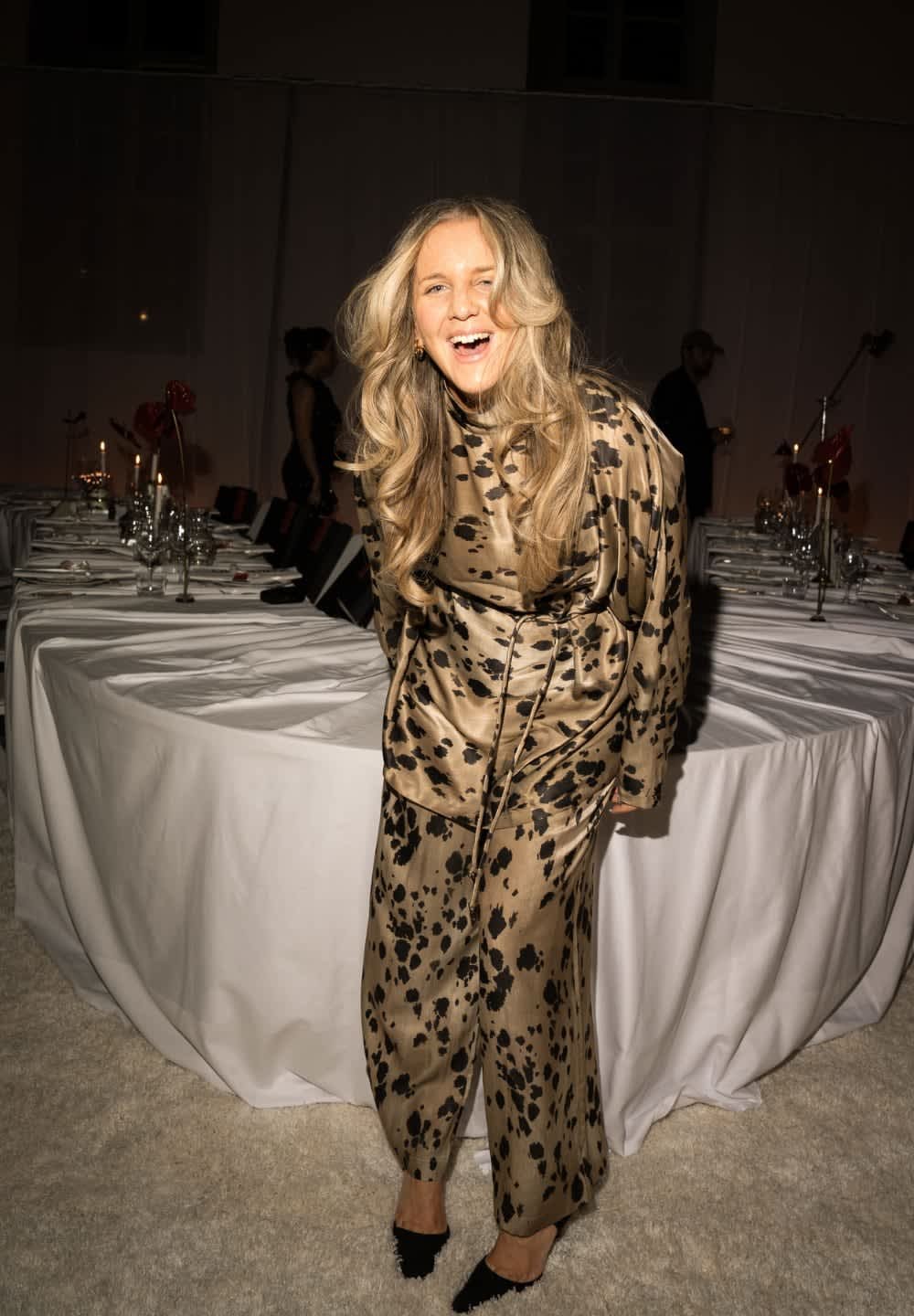 Guldsatinoutfit med svart djurmönster; består av en lös topp och vida byxor; stylad med svarta spetsiga skor.