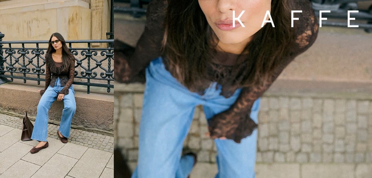 Kvinde iført en gennemsigtig sort top og blå jeans sidder udendørs på en stenreling nær et dekorativt sort metalgelænder.