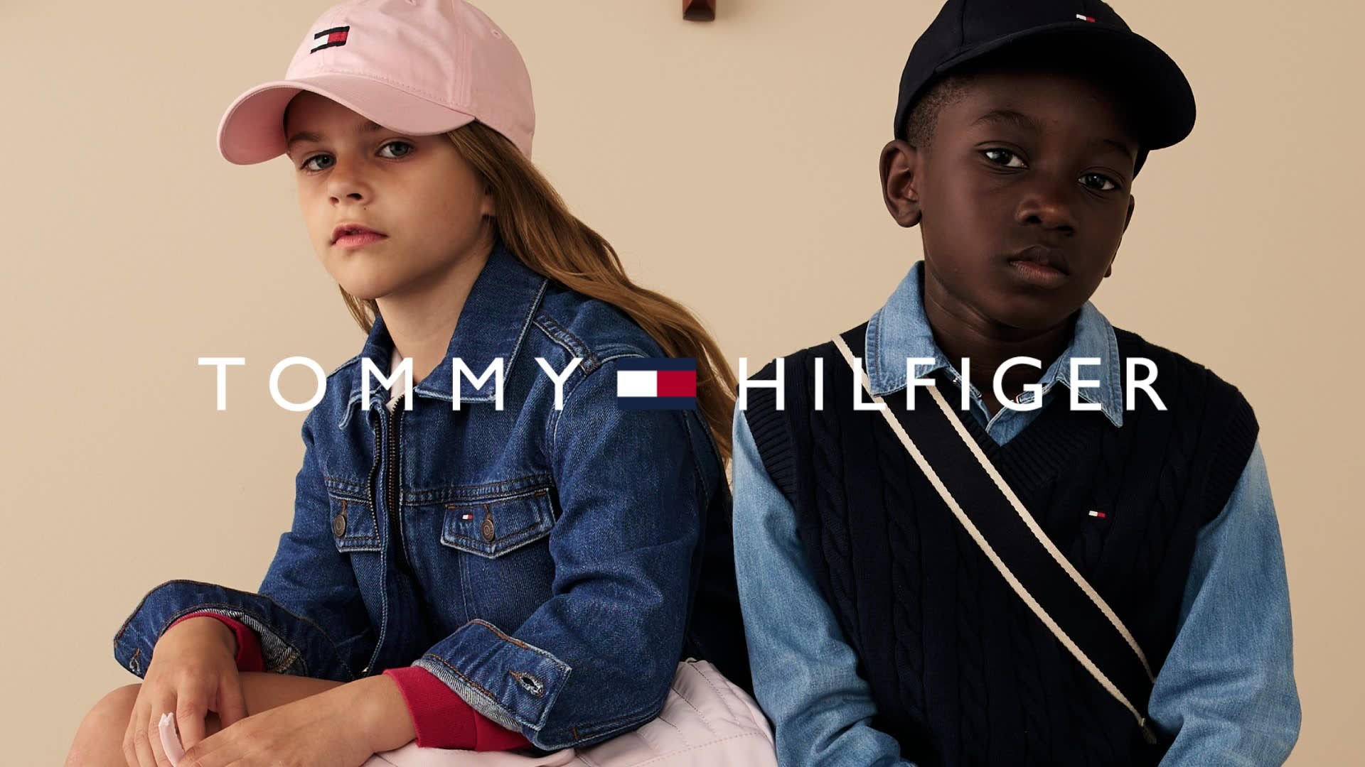 Giacca di jeans e cappellino rosa su un bambino; un gilet di maglione navy sopra una camicia azzurro chiaro su un altro. Logo visualizzato centralmente.
