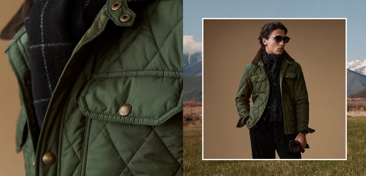 Homme portant une veste matelassée verte, une écharpe noire, un pantalon noir et des lunettes de soleil, tenant des gants bruns, se tenant devant un fond beige.