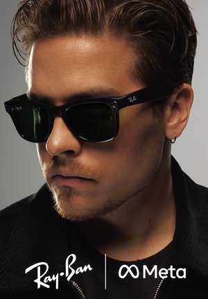 Zwarte Ray-Ban zonnebril met donkere lenzen, voorzien van een rechthoekige vorm en metalen accenten. Het model heeft kort haar en een lichte baard.