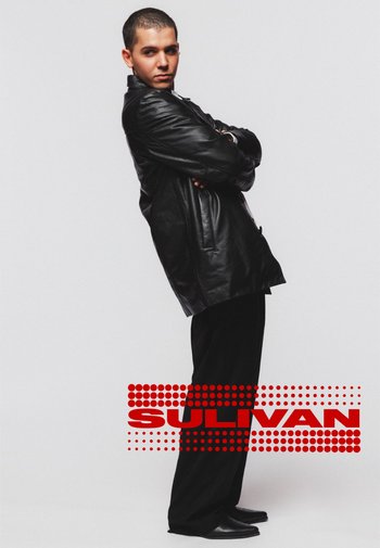 Veste en cuir noire à coupe décontractée, accompagnée de pantalons larges noirs et de chaussures noires à bout pointu ; un texte rouge superposé indique "SULIVAN."
