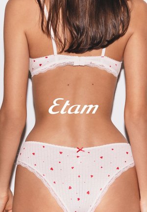 Dos d'une femme portant une lingerie blanche avec de petits cœurs rouges, ornée d'une bordure en dentelle et d'un nœud rouge sur la culotte, avec le texte "Etam" en superposition.