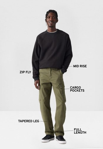 Hombre vestido con sudadera negra y pantalones cargo verde oliva con piernas ajustadas, cremallera, tiro medio, bolsillos cargo y longitud completa.