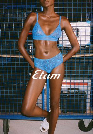 Light blue lace bralette with adjustable straps, paired with matching high-waisted brief. Features intricate patterns. Set against a blue storage backdrop.
