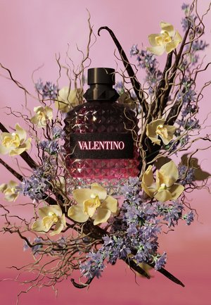 Valentino Parfümflasche umgeben von gelben Orchideen, violetten Blumen und verdrehten Zweigen auf rosa Hintergrund.