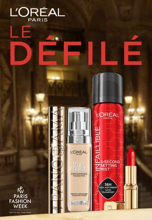 Fire L'Oréal Paris produkter: en gylden cylindrisk foundation, en klar serum pump, en rød setting mist og en rød læbestift. Baggrunden har prangende dekorationer.