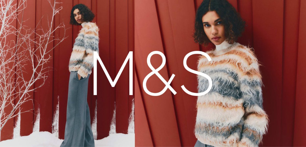 Miękki sweter w poziome paski w kolorach kremowym, pomarańczowym i niebieskim, zestawiony z szarymi spodniami z wysokim stanem i szerokimi nogawkami. Tło jest czerwone.