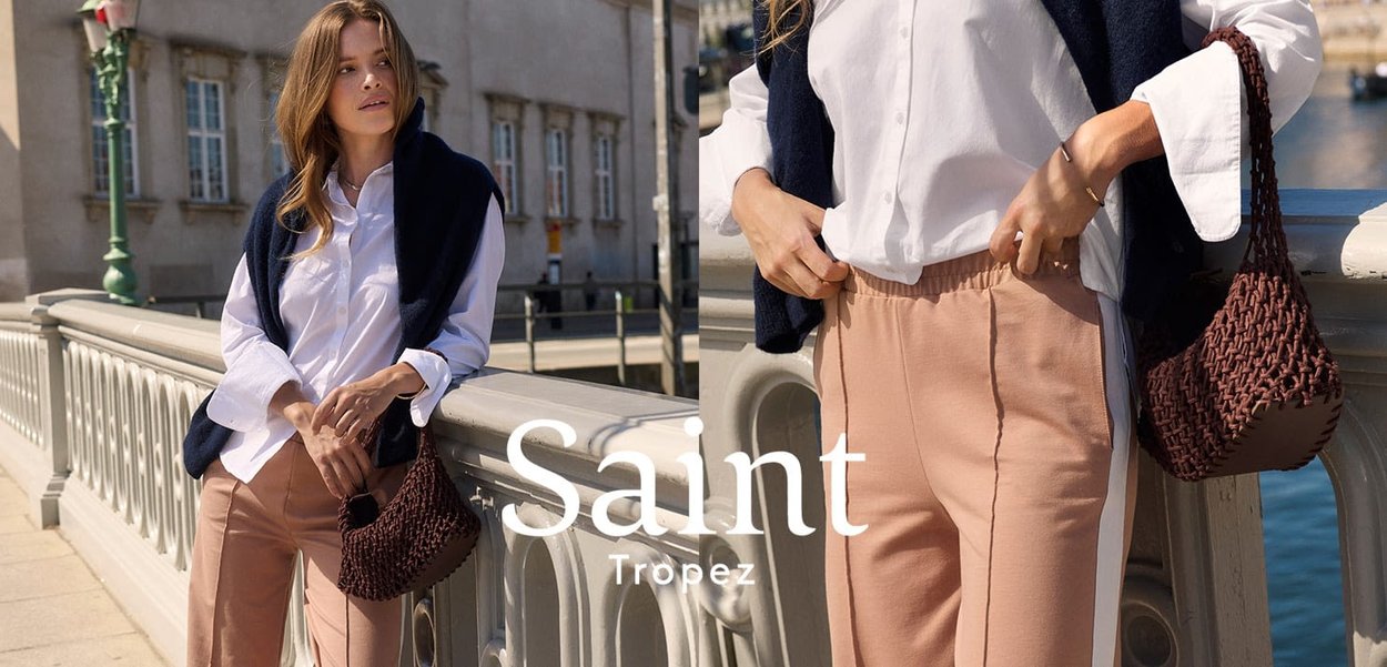 Camicia bianca a maniche lunghe, maglione senza maniche blu navy, pantaloni a sigaretta rosa con righe laterali e una borsa intrecciata marrone su uno sfondo sfocato.