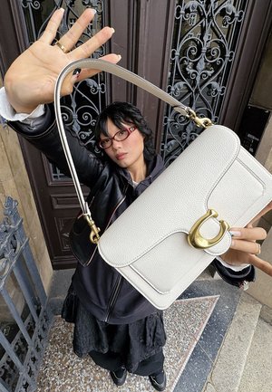 Borsa a tracolla bianca in pelle con finitura strutturata, dettagli in metallo dorato e design strutturato. Presenta una spallina singola e una patta rotonda.