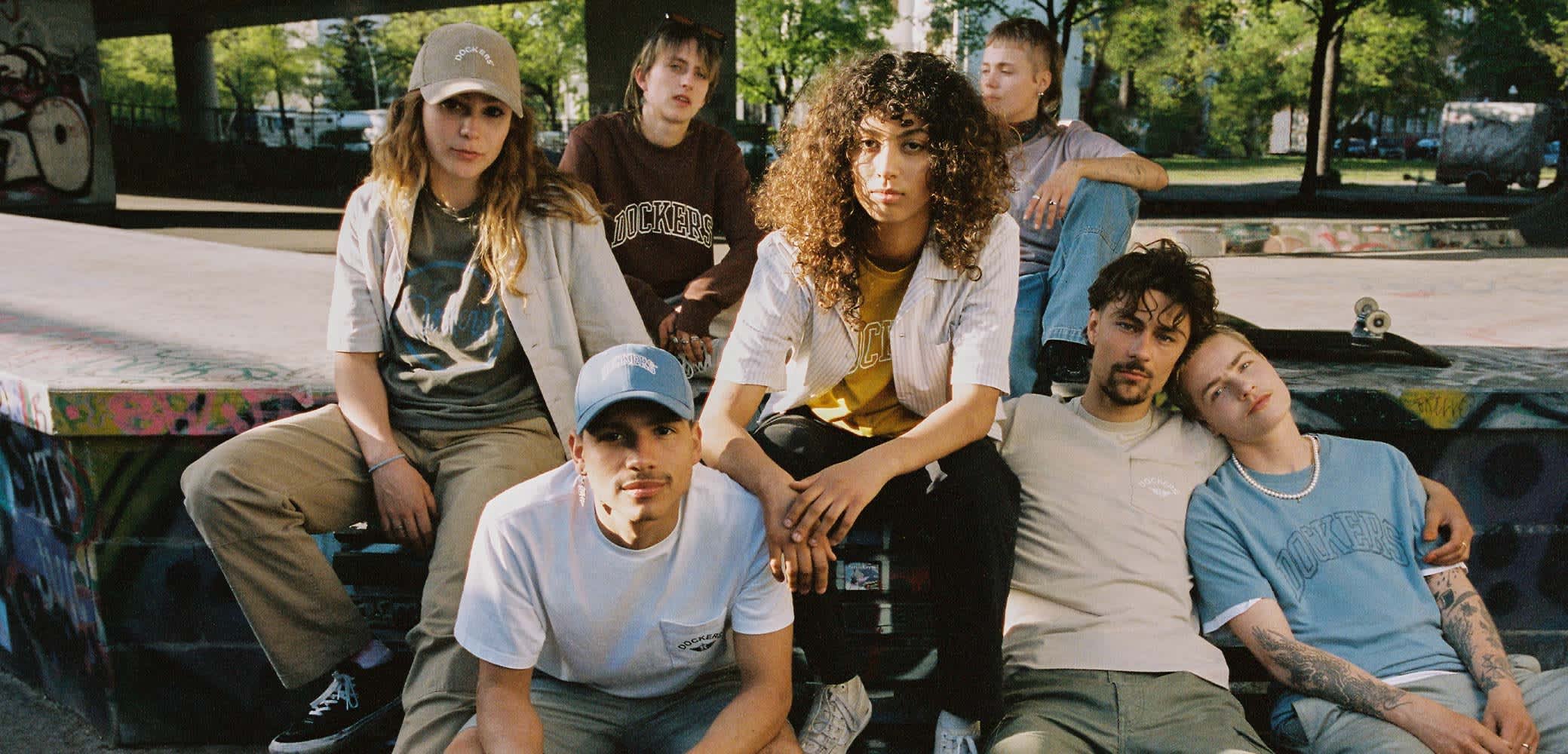 Sept individus sont assis sur une rampe de skate, portant des vêtements décontractés de rue de différentes couleurs. Parmi les articles notables, on trouve des chapeaux, des t-shirts graphiques et du denim.