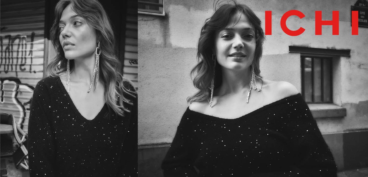 Schwarzer Pullover mit schulterfreiem Design, verziert mit silbernen Pailletten. Kombiniert mit langen, hängenden Ohrringen. Hintergrund zeigt urbanes Graffiti.