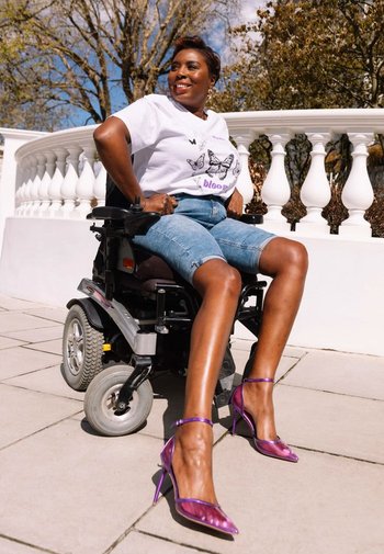 Lila öppna klackar med klara remmar, bärs med denimshorts och en vit T-shirt med en fjärilsdesign, sittande i rullstol.