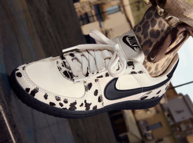 Nike Sneakers in Weiss mit schwarzen Leopardenflecken, ausgestattet mit einem schwarzen Swoosh, weißen Schnürsenkeln und einer strukturierten Oberfläche. Schwarze Gummisohle.