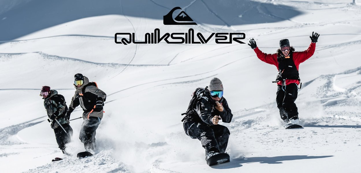 Zwei Snowboarder auf verschneitem Gelände. Einer in schwarzer Ausrüstung, grauer Mütze, verspiegelten Skibrillen; der andere in Rot, mit schwarzer Weste, die Hände freudig erhoben.