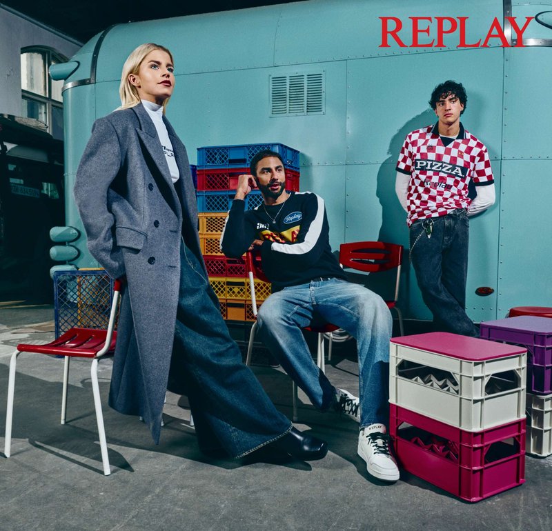 Tre modelli sono vestiti con abbigliamento casual: un cappotto grigio, una maglietta sportiva bianca e nera, e una camicia a quadri rossi. Vicino ci sono delle casse di plastica colorate.