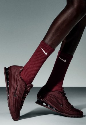 Zapatillas Nike burdeos con parte superior de malla texturizada, que cuentan con una suela curva y amortiguación de aire transparente. Combinadas con calcetines acanalados a juego.