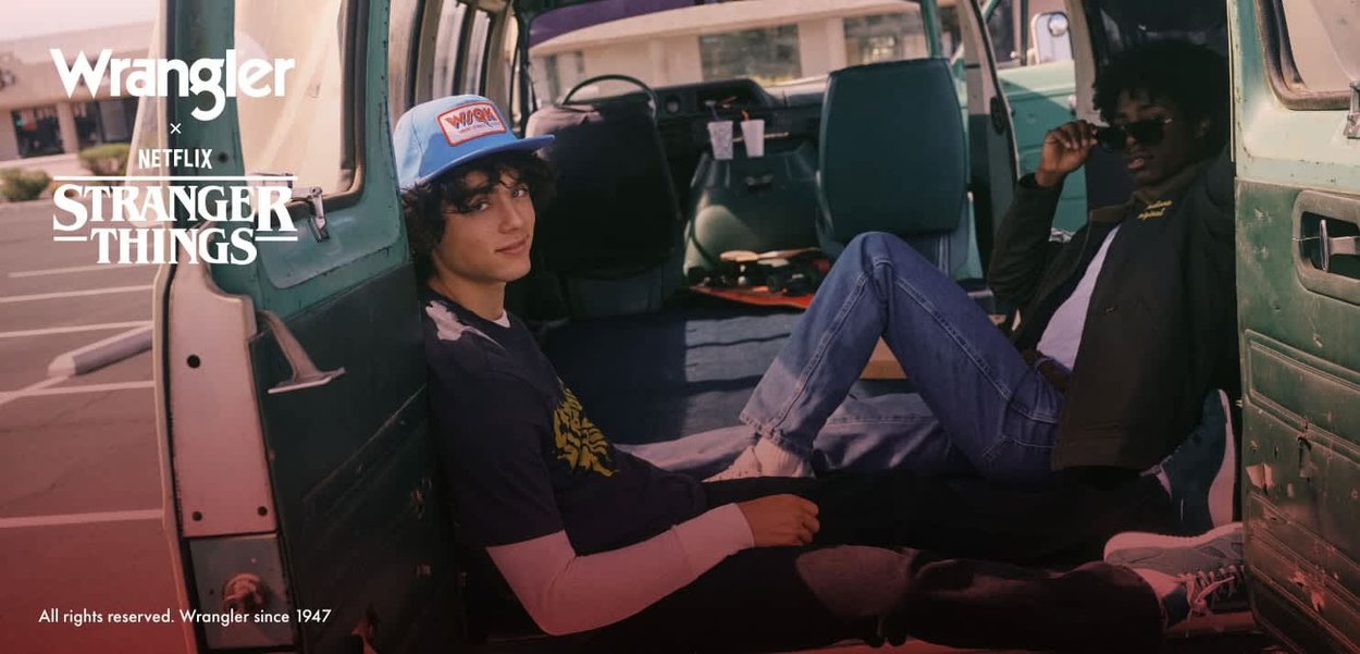 Wrangler x Stranger Things-samarbeid som viser to personer avslappet i en vintage grønn varebil, med avslappede klær og tilbehør.