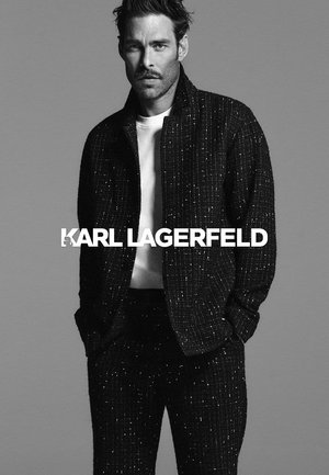 Costume en tweed noir avec des accents en fil métallique. Comprend une veste texturée et un pantalon assorti, porté sur un t-shirt blanc.