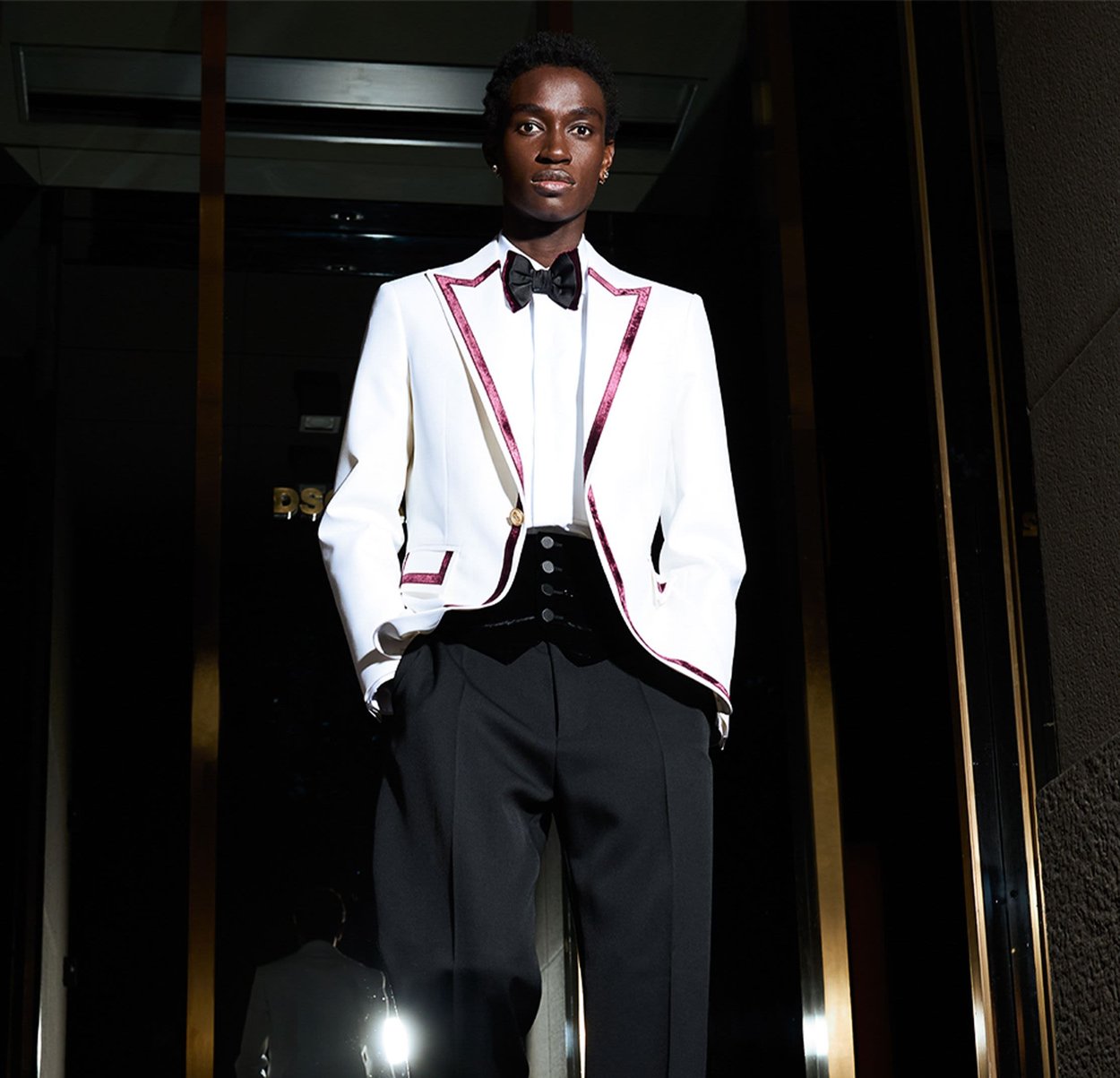 Chaqueta de esmoquin blanca con ribete burdeos, chaleco negro, pantalones negros y pajarita. Tejido suave, diseño estructurado y silueta ajustada.