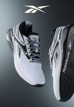 Wit-zwart Reebok hardloopschoenen met patroon veter, waarvan de ene van bovenaf te zien is en de andere de zool met het Reebok-logo laat zien.
