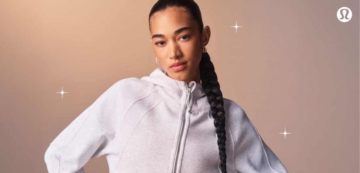 Sweat à capuche gris zippé avec un col haut, doté de manches raglan et d'une texture lisse. Le modèle arbore une longue coiffure tressée.