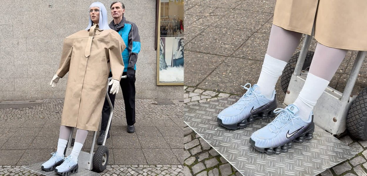 En mannequin iført en beige frakke står på en dolly, iført blå Nike fodboldstøvler, hvide sokker og grå leggings på en tekstureret belægning.