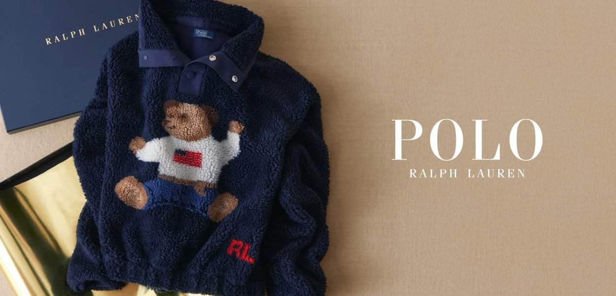 Laivastonsininen fleeceneule, jossa on nallekarhukuosi teksturoidulla pistolla. Neuleessa on kaulus, jossa napit, ja punainen "R"-kirjain.