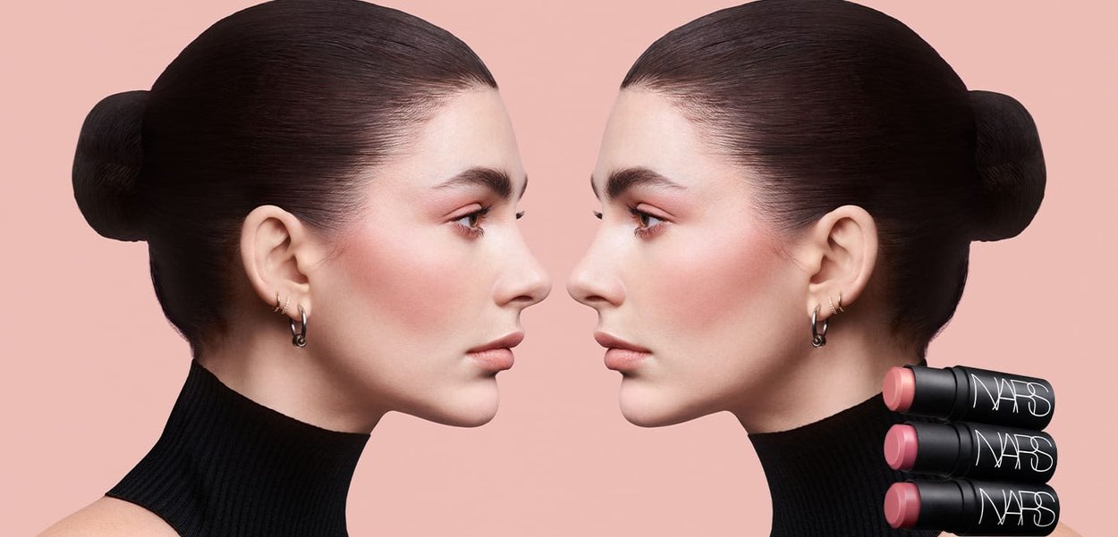 Rossetti NARS esposti accanto a due volti identici con capelli tirati indietro, che mostrano una pelle liscia, blush e tonalità neutre su uno sfondo rosa.
