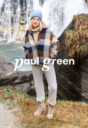 Plaid jacket in blue, orange, and cream, with a faux fur collar; beige ribbed pants; tan lace-up boots; waterfall in background.