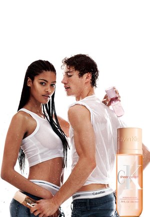 Ein Mann und eine Frau in nassen weissen Tops und Calvin Klein Unterwäsche stehen nah beieinander und halten pinke und pfirsichfarbene Calvin Klein Parfümflaschen.